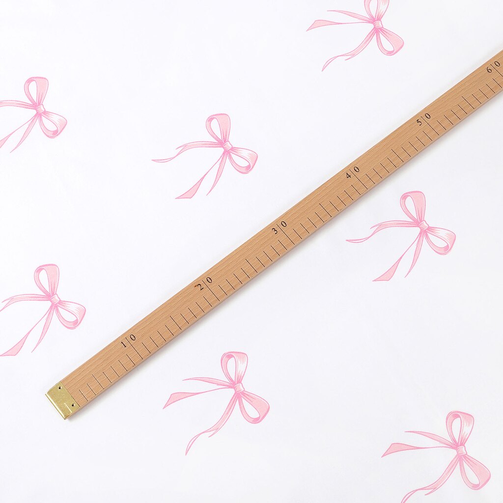 Pink bow cotton fabric shown with a centimetre ruler to demonstrate the motif size and pattern repeat