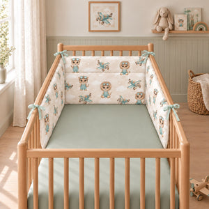 Safari Pilot bumper with soft mint ties in a natural wooden cot, styled with a sage green fitted sheet in a Scandinavian nursery.