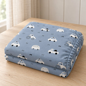 Folded blue cotton baby fitted sheet with white cars, tractors and buses, showing the elasticated edge on a light oak table.